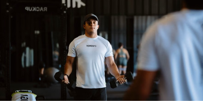 A man holding dumbbells in front of a mirror, checking his curl