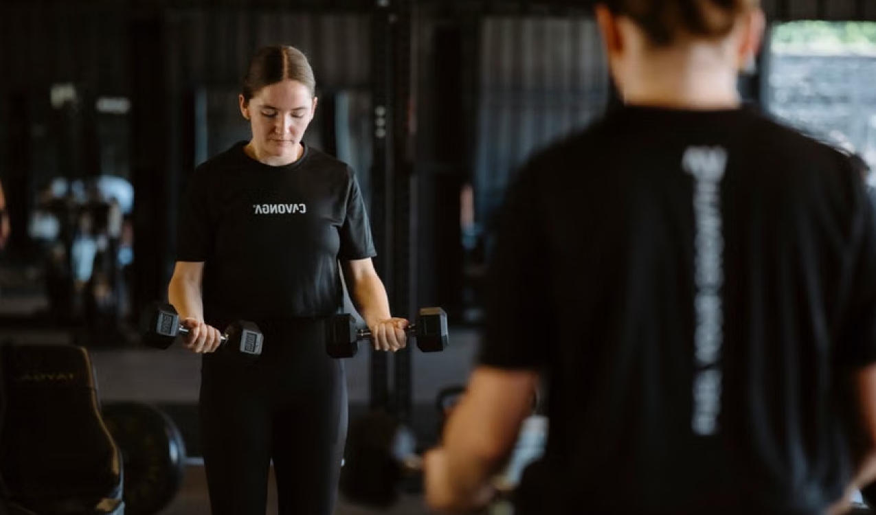 A woman doing a dumbbell curl while watching her form in a mirror